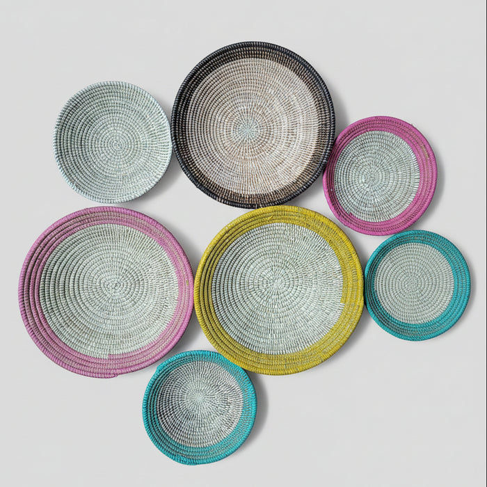 Six round woven baskets in various colors and sizes . The bowls feature a spiral woven pattern with rims in pink, yellow, teal, black, and white.