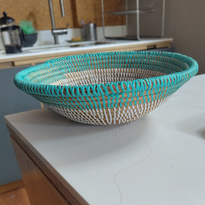 A woven oval basket with turquoise blue and natural beige stripes sits on a white kitchen countertop.