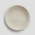 A round woven straw bowl in a light beige and white color.