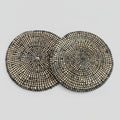 A set of two round placemats with a geometric pattern, featuring a mix of black and beige river grass with white binding.