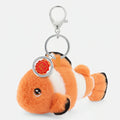 A plush clownfish keychain charm with orange and white stripes, black-tipped fins, a silver lobster clasp, and a round red-and-gold tag, shown on a plain white background.