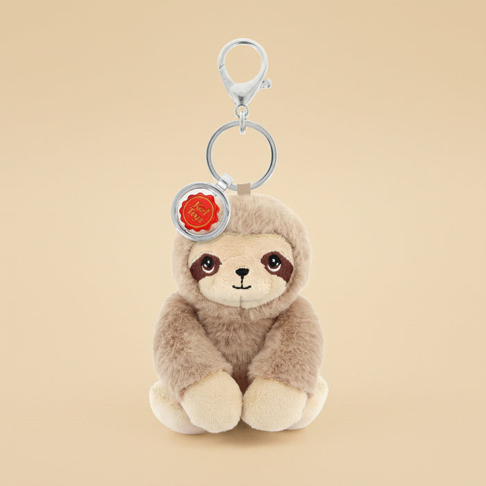 A plush sloth keychain charm with a silver metal clasp and key ring, featuring a light brown and cream sloth face with a small red circular tag.