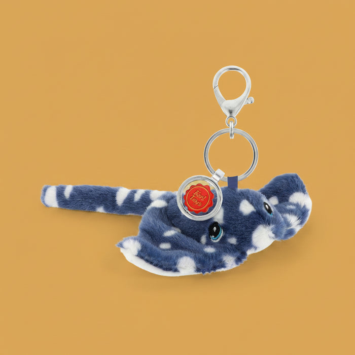 A plush keychain , a blue and white stingray, featuring a silver metal clasp, key ring, and a round red charm with a gold emblem.