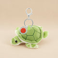 A plush green turtle keychain with a silver metal clasp and a round silver tag featuring a red seal, shown on a plain white background.