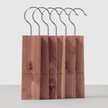 Five cedar wood bocks with black metal hooks, arranged in a row on a white background. Each stand has a vertical wood panel with a circular logo and the text 'STOCKING HANGER'.