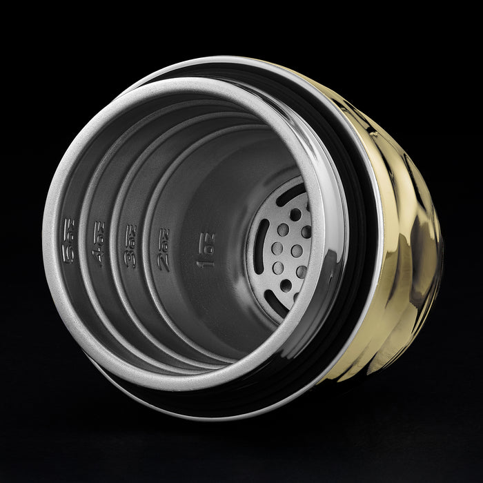 Close-up of a metallic hexclad cocktail shaker container with gold color rim and black interior on a black background