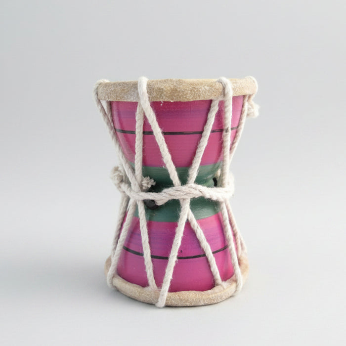 A small hand drum with a pink body, green and red stripes, and a beige-colored head, tied with a white rope.