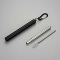 A  portable metal folding straw case. Shown on a grey surface, with a carabiner clip, plus a long metal straw and a small brush.