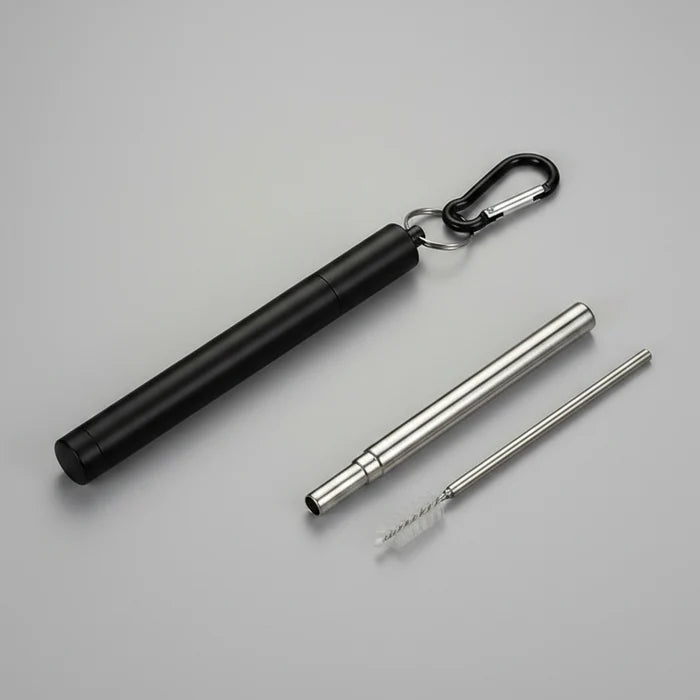 A  portable metal folding straw case. Shown on a grey surface, with a carabiner clip, plus a long metal straw and a small brush.