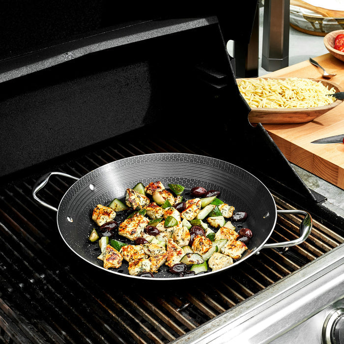 Pieces of chicken and vegetables being cooked in the HexClad 12&quot Hybrid BBQ Grill Pan on top of a grill
