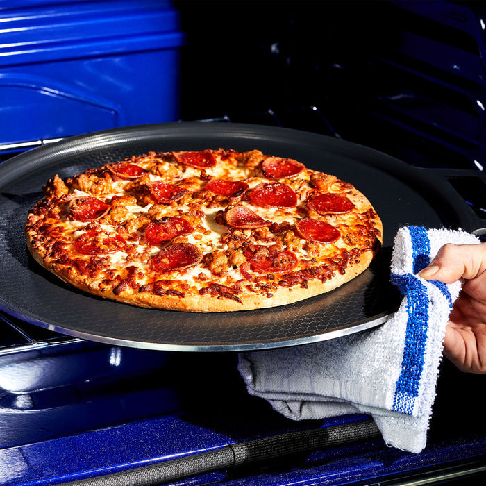 A hand taking a pepperoni pizza out of the oven on the HexClad hybrid pizza steel