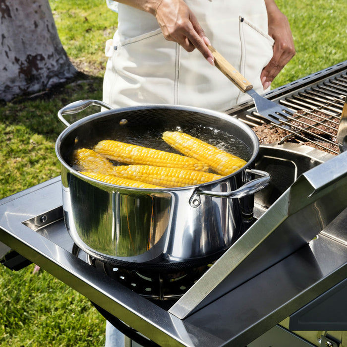 Someone using an outdoor grill, with a bowl of corn on the cob to the side.