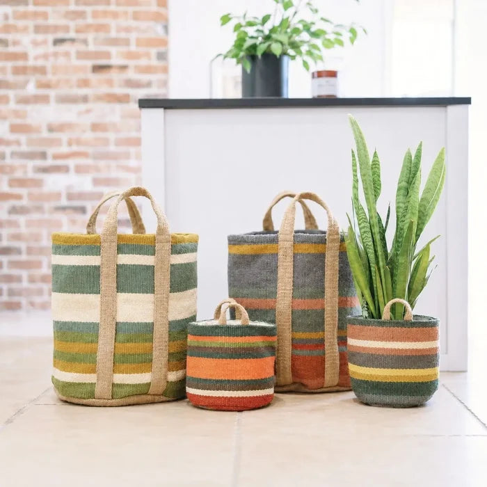 Four woven storage baskets in striped patterns in green, beige, orange, and gray, including two tote bags and two planters, arranged on a tiled floor in a bright room.