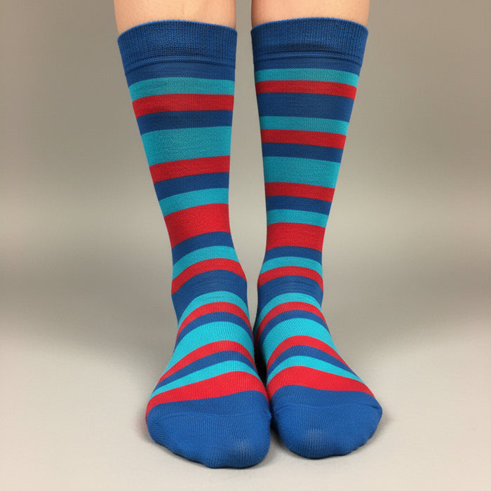 A pair of crew socks with horizontal stripes in blue, teal, and red, worn on a person's feet against a neutral gray studio background.