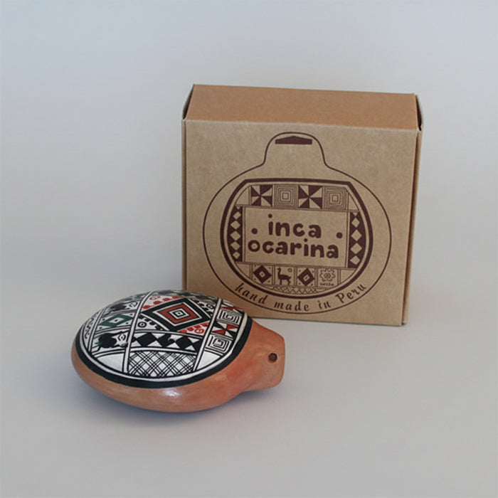 A handcrafted Inca Ocarina clay whistle with a black, red, and white geometric pattern on a terracotta base, shown in front of its brown cardboard packaging box on a white background.