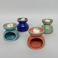Six small ceramic wax melts or scented candle holders in assorted colors, arranged on a patterned fabric surface against a plain white wall.