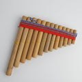 A traditional wooden pan flute instrument with multiple natural bamboo tubes arranged in a triangular shape, bound with a red cord and a blue-and-white patterned strap, shown on a plain white background.