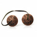 Two bronze-colored Tibetan prayer bells connected by a leather cord, with intricate designs on the bells.