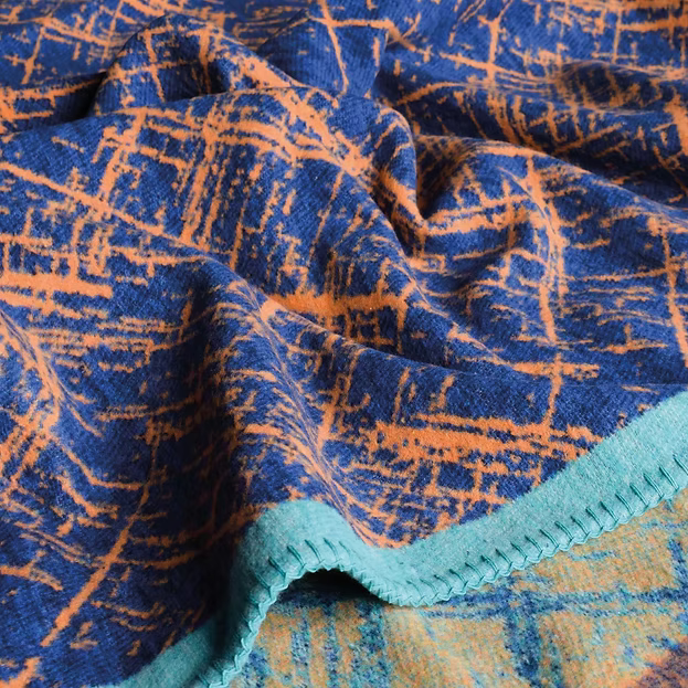A close-up of a knitted fabric with a blue and orange abstract pattern, finished with a teal ribbed trim.