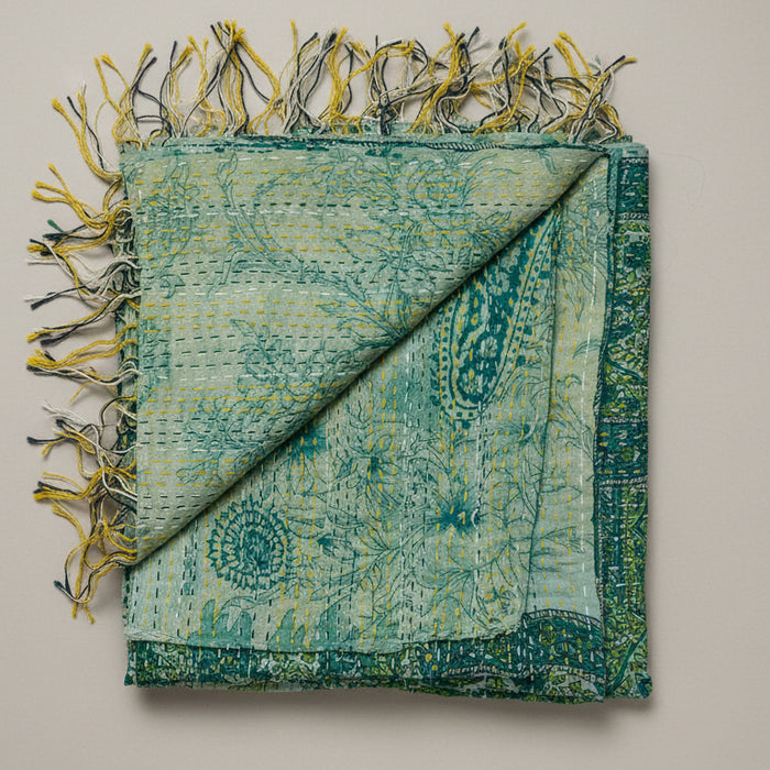 Green and beige patterned scarf with fringes on a textured white background