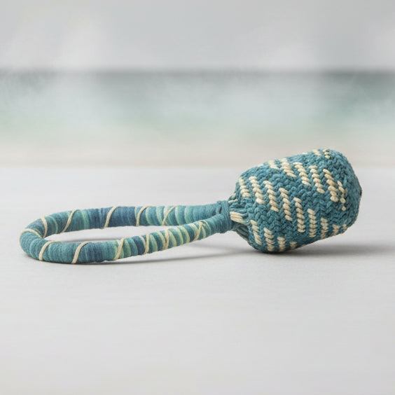 A handwoven straw rattle with a bell, featuring a green and natural-colored pattern.