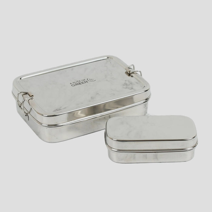 Two silver metal lidded lunch boxes, one larger tin showing the brand name 'Made by GREEN' and one smaller tin, set against a light gray background.
