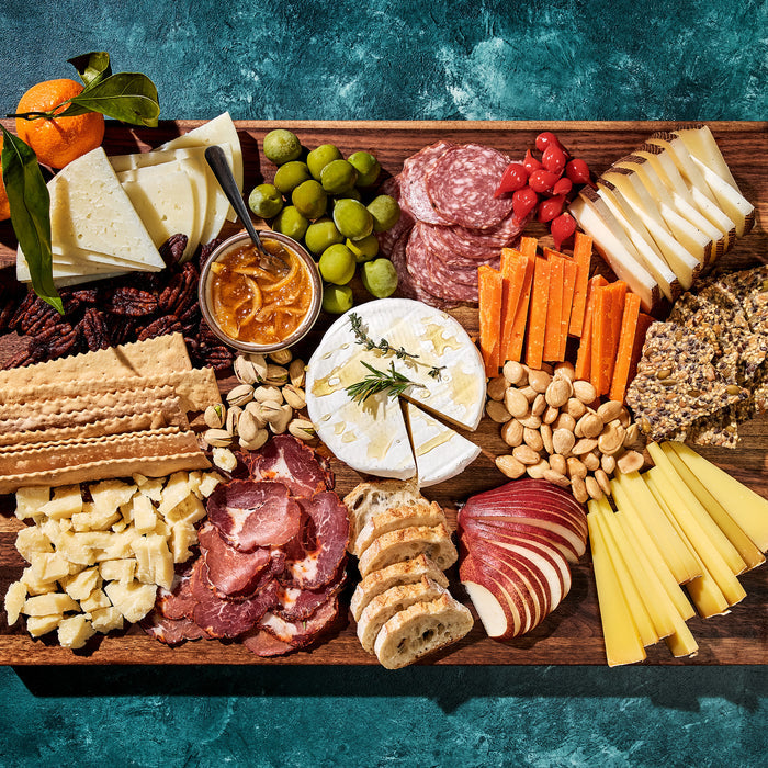 A charcuterie board of meats, cheeses, fruit, and spreads on a wooden cutting board.